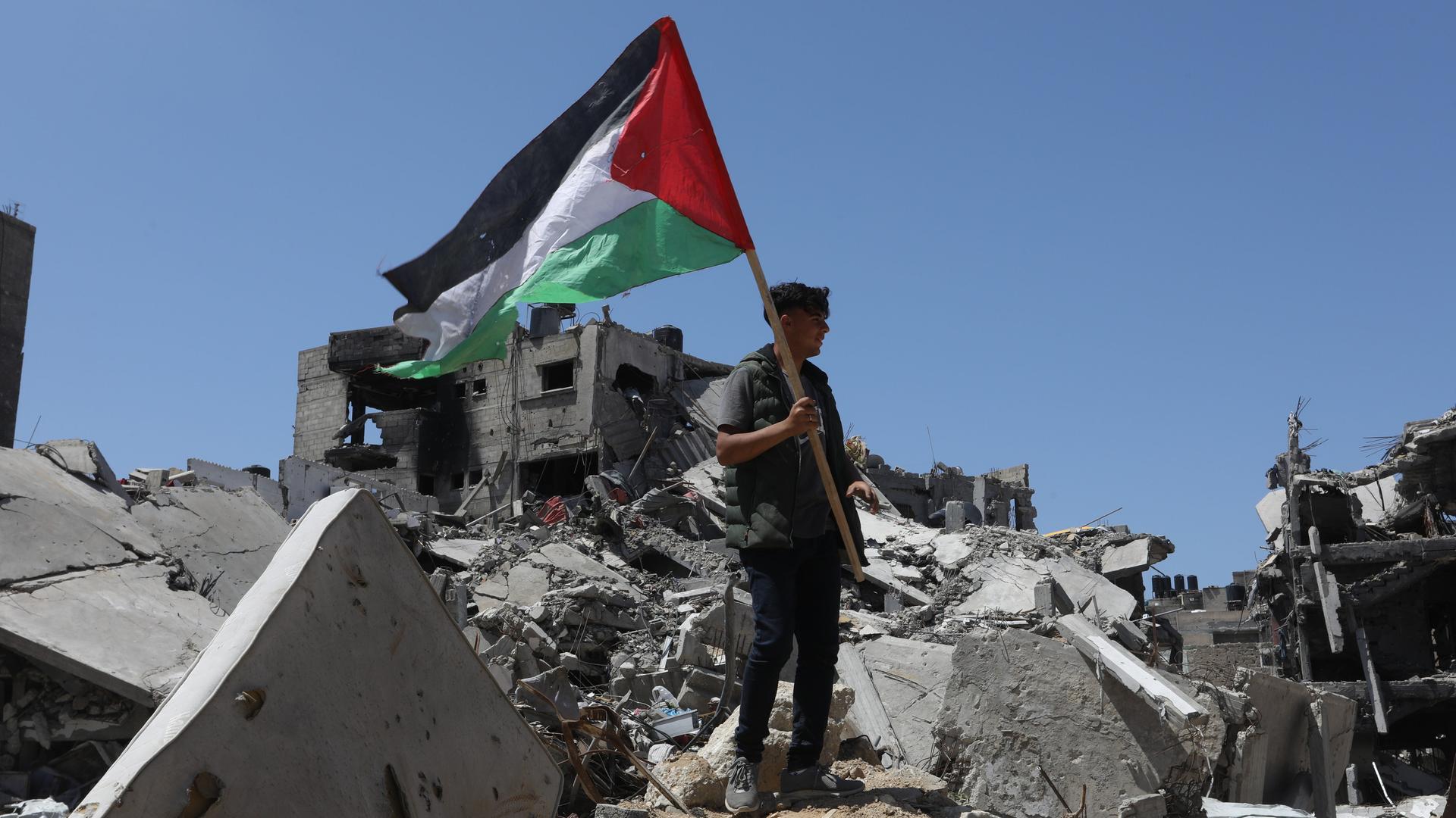Ein palästinensischer Mann hält die palästinensische Flagge in der Hand, während er auf den Trümmern steht, die durch israelische Bombardements im Rahmen des israelischen Krieges gegen Gaza verursacht wurden. Ein palästinensischer Mann hält die palästinensische Flagge in der Hand, während er auf den Trümmern steht, die durch israelische Bombardements im Rahmen des israelischen Krieges gegen Gaza verursacht wurden.