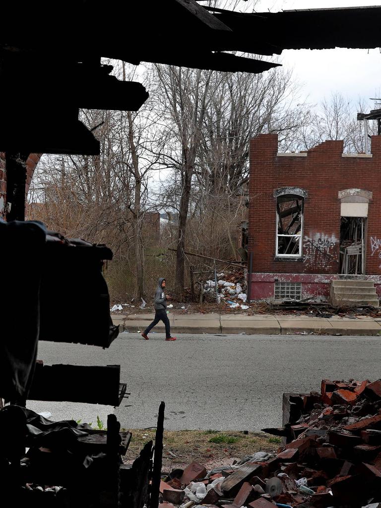 Ein Mann läuft eine Straße entlang. Auf der gegenüberliegenden Straßenseite verfällt ein leerstehendes Wohnhaus. 