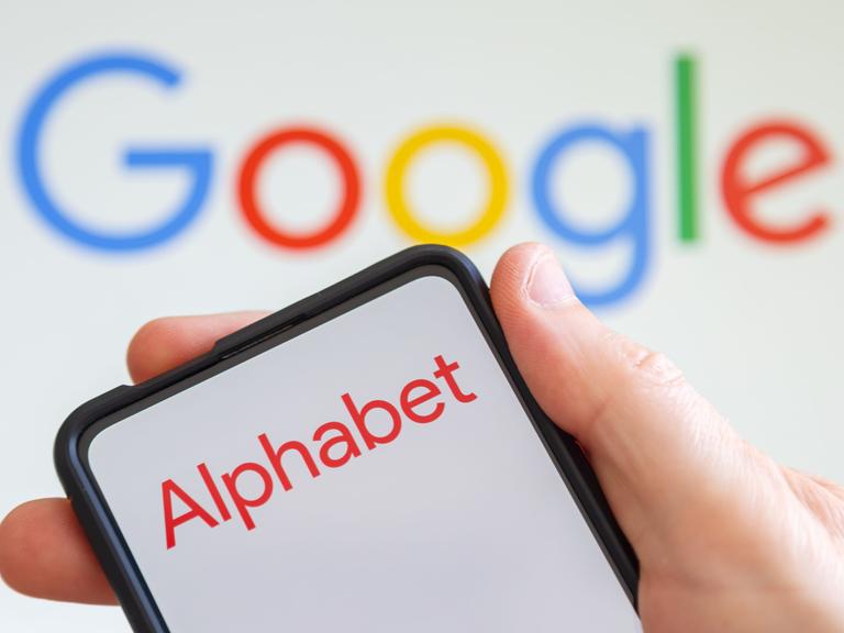 Logo von Alphabet auf einem Smartphone, dahinter das Google-Logo.