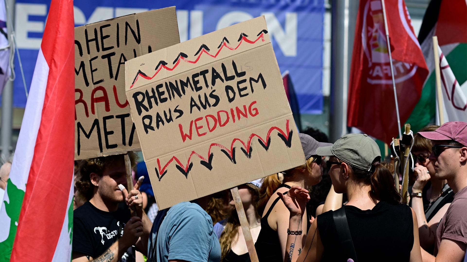 Mehrere Demonstranten stehen nebeneinander. Eine Person hält ein Schild mit der Aufschrift "Rheinmetall raus aus dem Wedding" in die Höhe.