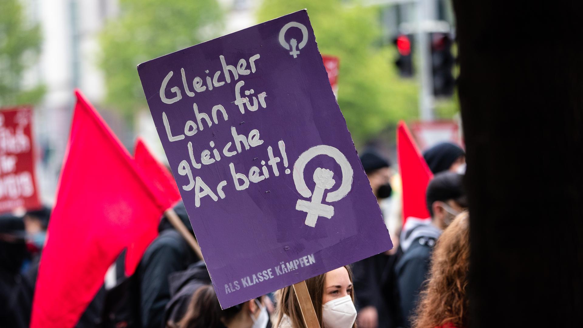 Eine Demonstrantin hält ein Plakat mit der Aufschrift "Gleicher Lohn für gleiche Arbeit - Als Klasse kämpfen"