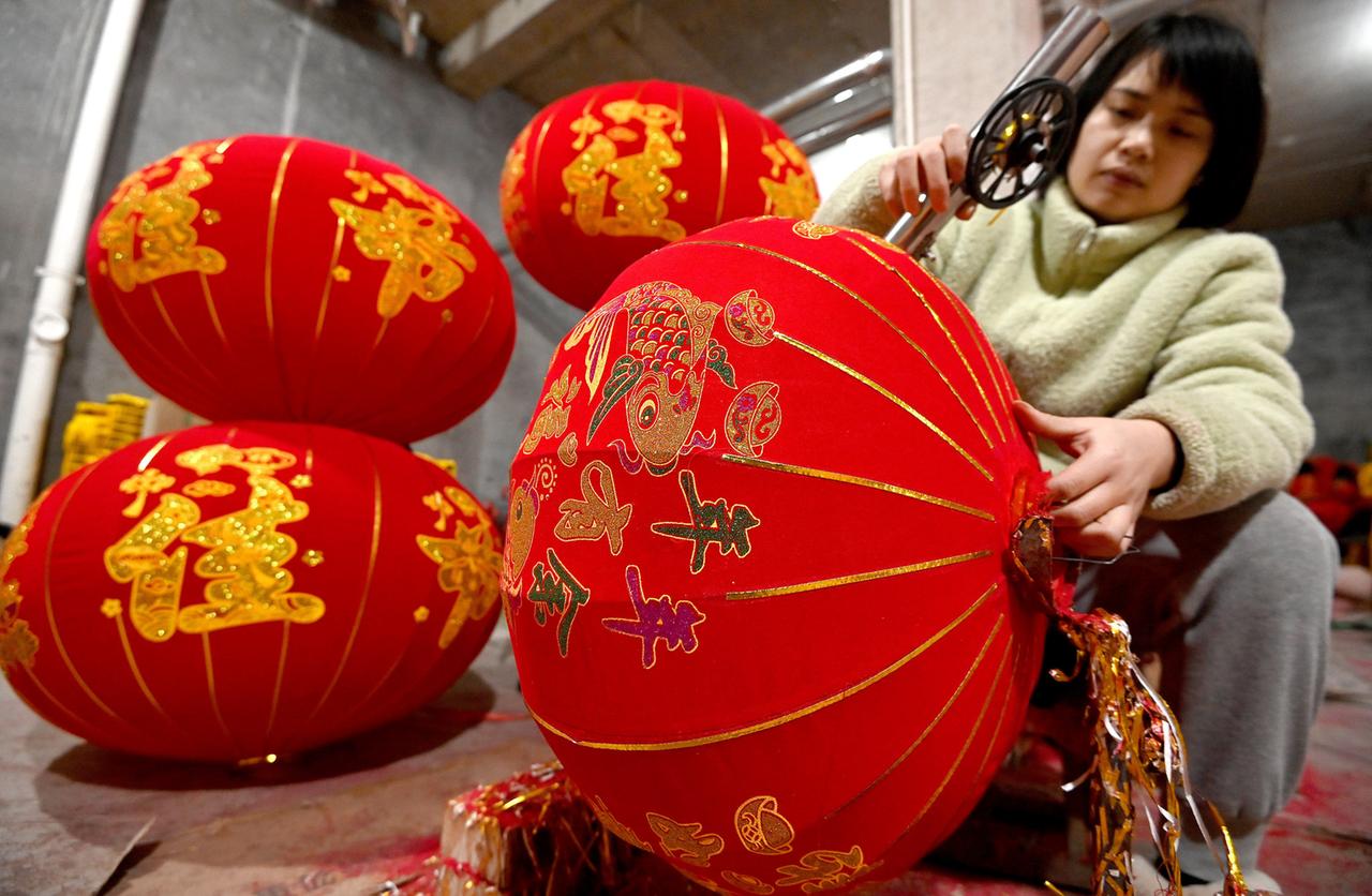 Eine Frau näht einen traditionellen roten Lampion, der zum chinesischen Neujahrsfest an vielen Häusern aufgehängt wird, um mit seinem Licht dem Glück den Weg zu weisen.