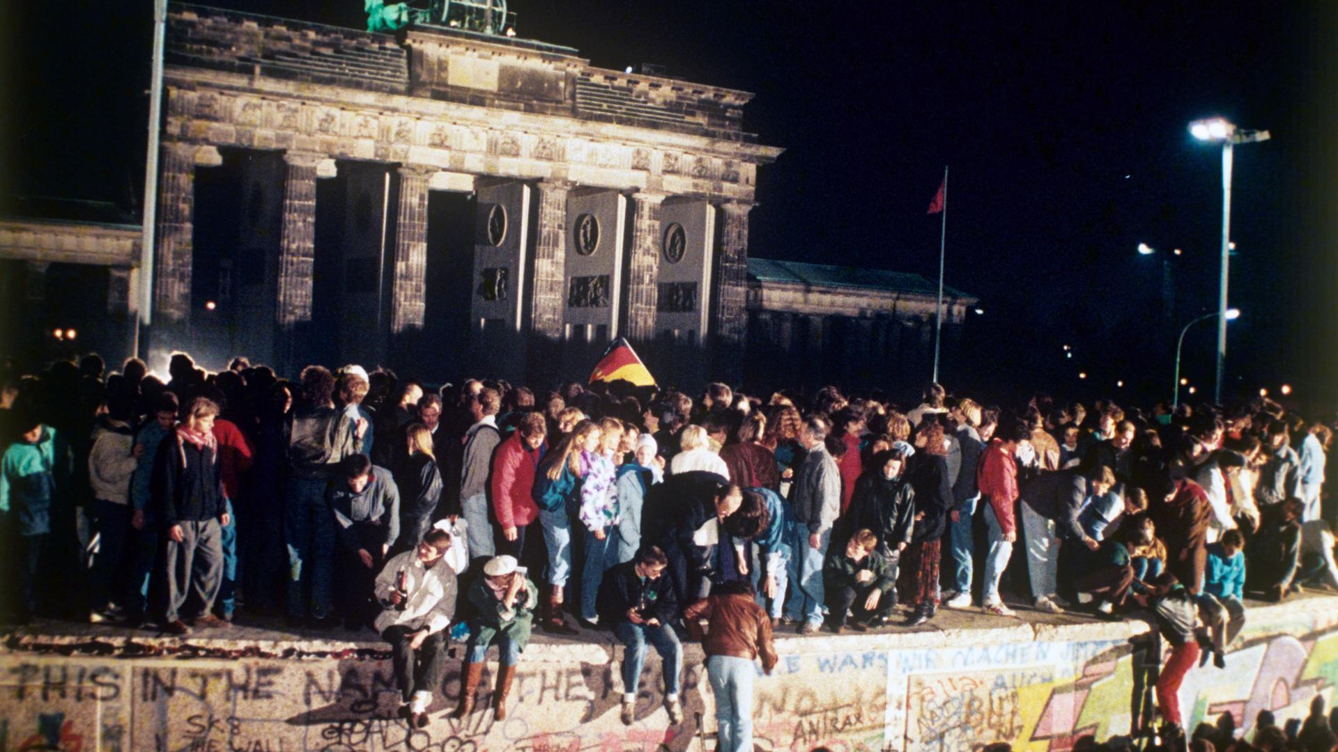 Jubelnde Menschen auf der Berliner Mauer vor dem Brandenburger Tor am 09.11.1989. Nach der Öffnung eines Teils der deutsch-deutschen Grenzübergänge reisten Millionen DDR-Bürger für einen kurzen Besuch in den Westen.