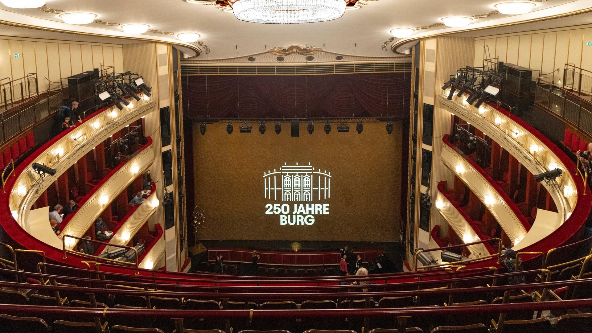 Die Bühne des Wiener Burgtheaters, vom obersten Rang aus gesehen. Zwischen dem roten Vorhang auf der Bühne steht auf einer Leinwand: "250 Jahre Burg" Die Bühne des Wiener Burgtheaters, vom obersten Rang aus gesehen. Zwischen dem roten Vorhang auf der Bühne steht auf einer Leinwand: "250 Jahre Burg"