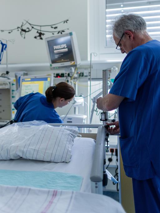 In einem Krankenhaus richten eine Pflegerin und Pfleger ein Intensivbett her.