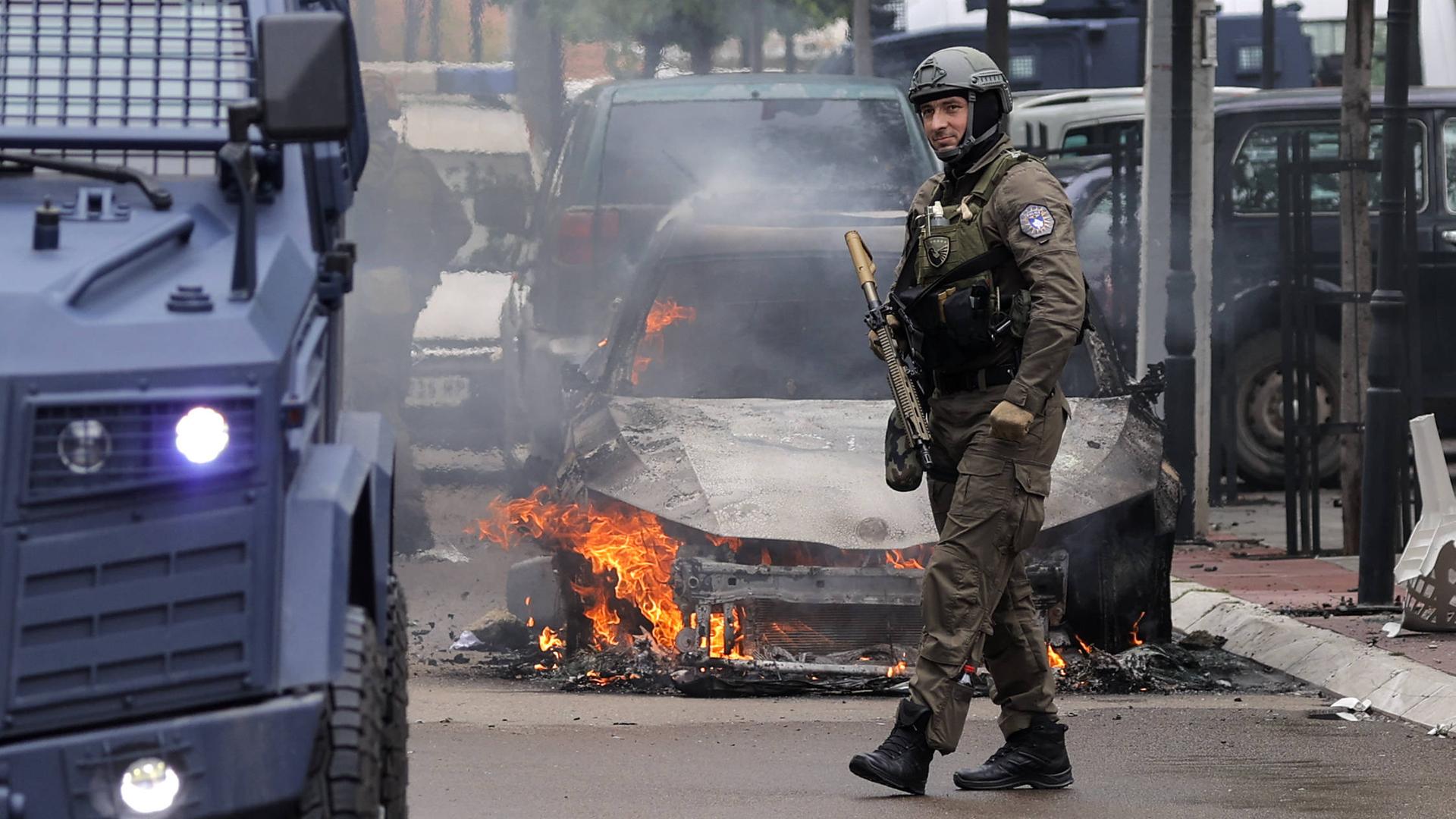 Ein Soldat vor einem ausgebrannten Auto