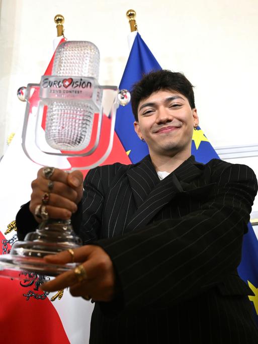 ESC-Sieger JJ zeigt die ESC-Trophae, dahinter die Flagge Österreichs und der EU 