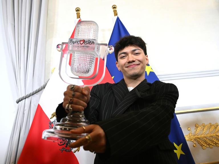 ESC-Sieger JJ zeigt die ESC-Trophae, dahinter die Flagge Österreichs und der EU 