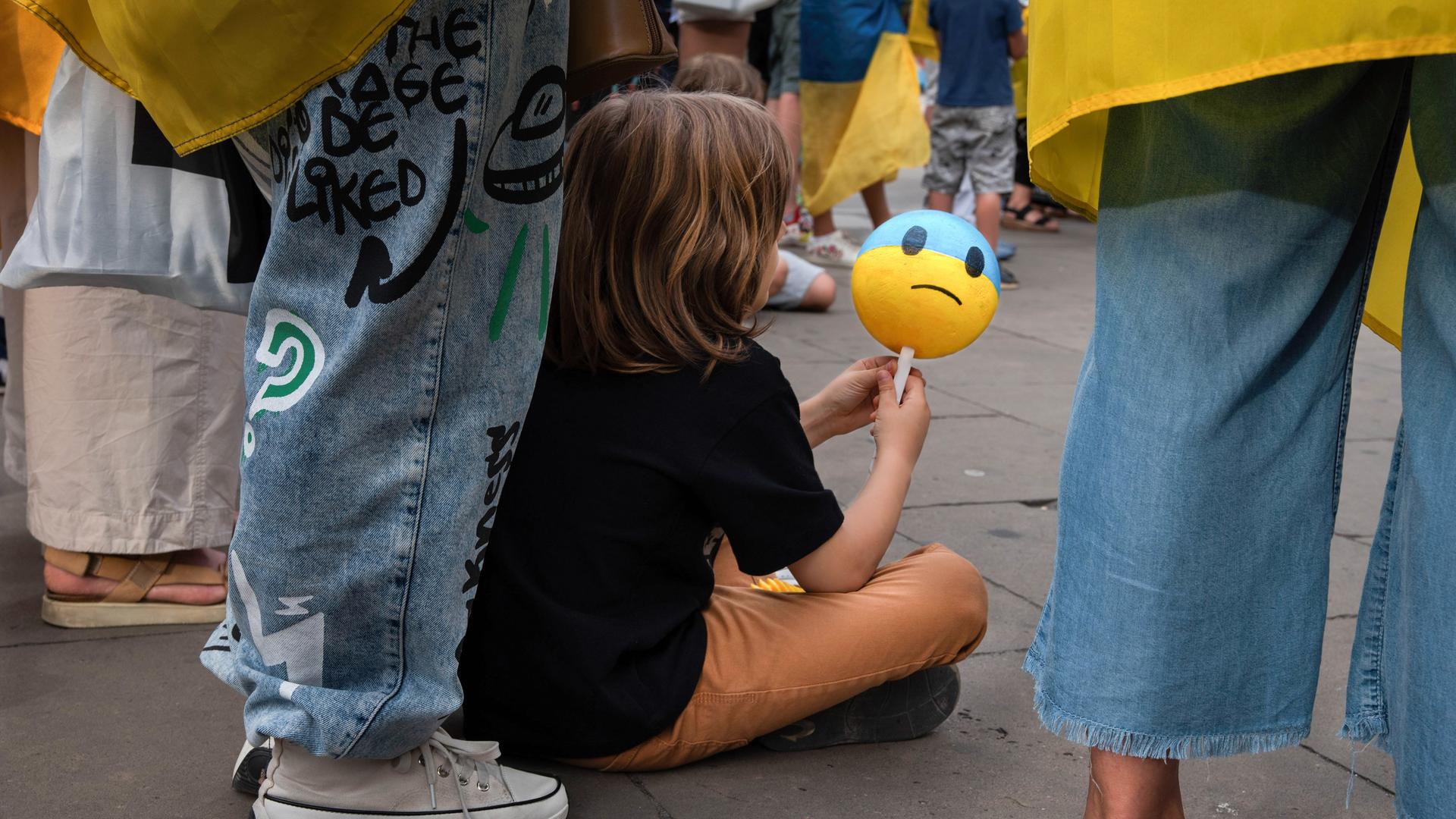 Ein Junge hält einen Ball mit einem traurigem Gesicht bei einer Demonstration in der Hand.