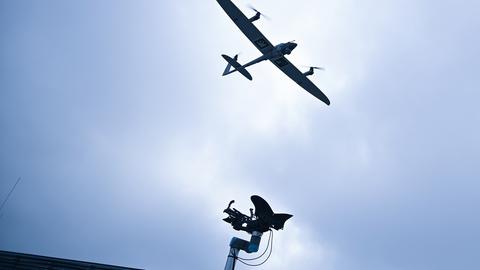 Am Himmel ist eine Drohne zu sehen. Am unteren Rand des Bildes ragt eine Sendeantenne ins Bild.