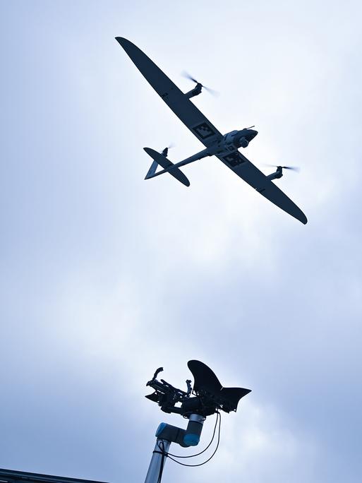 Am Himmel ist eine Drohne zu sehen. Am unteren Rand des Bildes ragt eine Sendeantenne ins Bild.