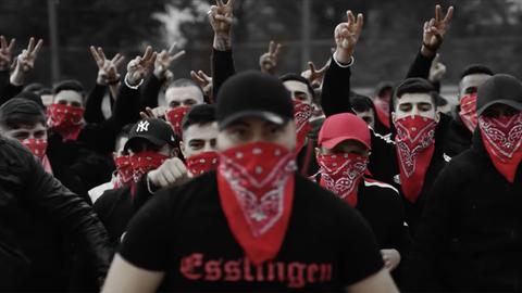 Screenshot aus dem Musikvideo "Eska - Bumaye". Eine Gruppe vermummter junger Männer mit der Aufschrift "Esslingen" auf schwarzer Kleidung. Rapper Eska wird mit einer Bande in Verbindung gebracht. In seinen Musikvideos inszenieren sich Männer als Gangster.