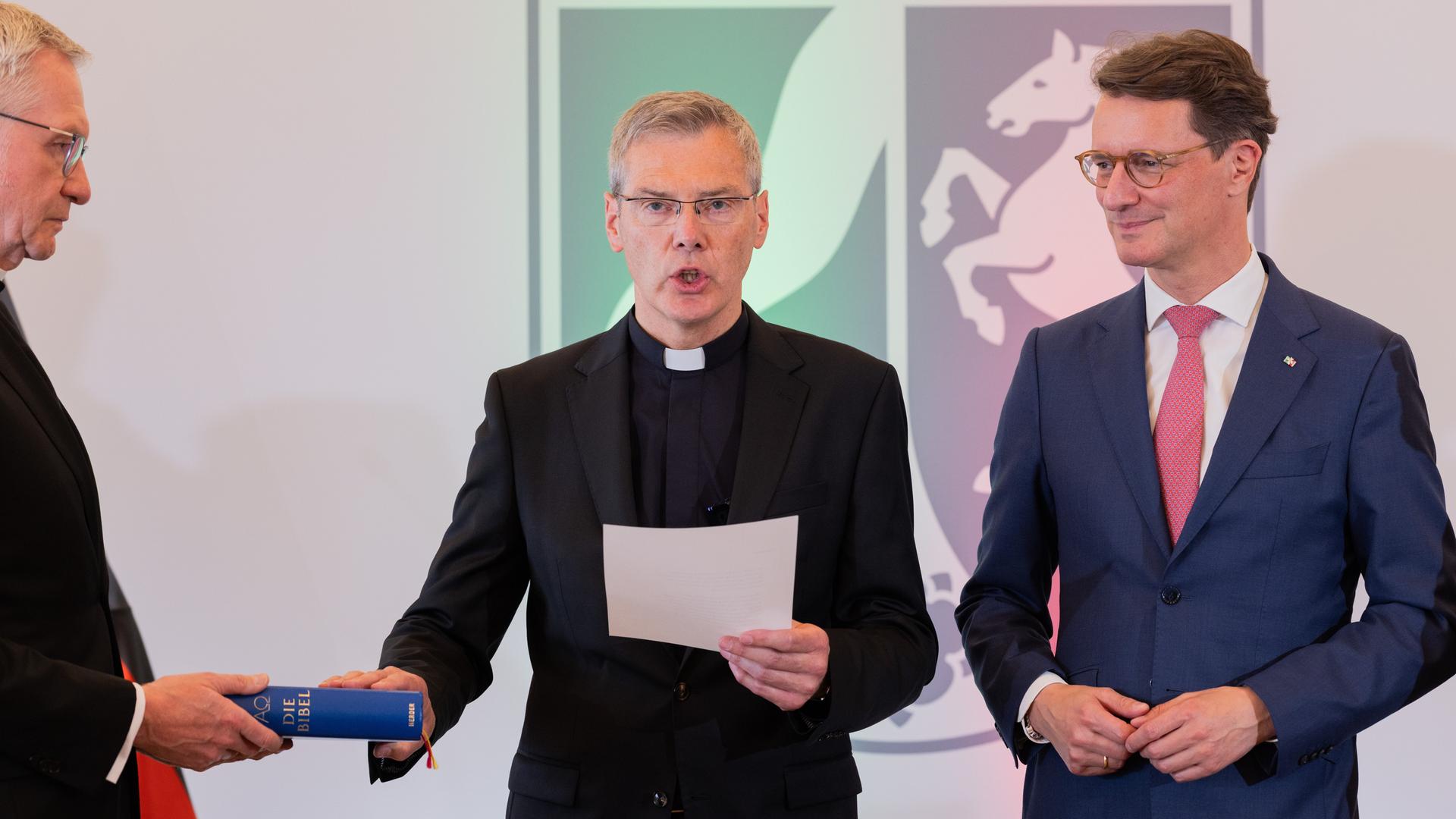 Heiner Wilmer (M), Bischof von Münster, legt bei seiner Vereidigung in der Staatskanzlei neben Hendrik Wüst (r, CDU), Ministerpräsident von Nordrhein-Westfalen, seine Hand auf eine Bibel. Heiner Wilmer (M), Bischof von Münster, legt bei seiner Vereidigung in der Staatskanzlei neben Hendrik Wüst (r, CDU), Ministerpräsident von Nordrhein-Westfalen, seine Hand auf eine Bibel.