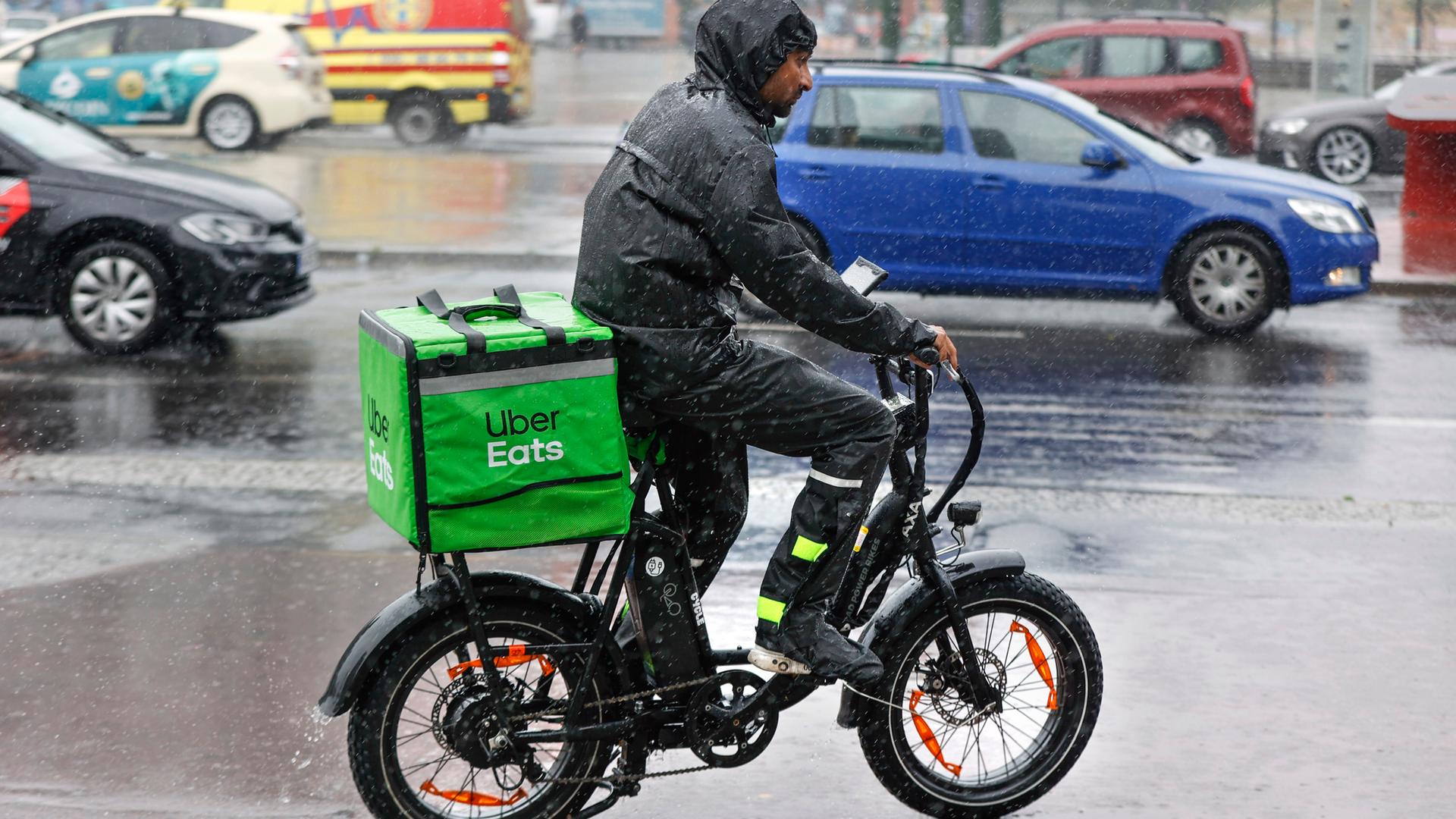 Ein Fahrer des Lieferdienstes Uber Eats fährt mit seinem E-Bike bei starkem Regen über eine Strasse. 