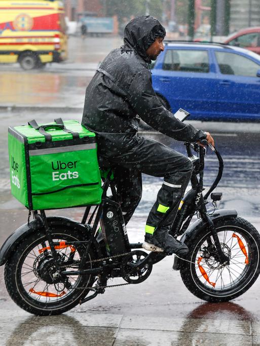 Ein Fahrer des Lieferdienstes Uber Eats fährt mit seinem E-Bike bei starkem Regen über eine Strasse. 