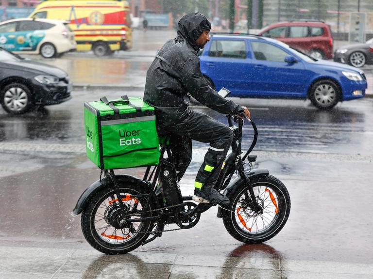Ein Fahrer des Lieferdienstes Uber Eats fährt mit seinem E-Bike bei starkem Regen über eine Strasse. 
