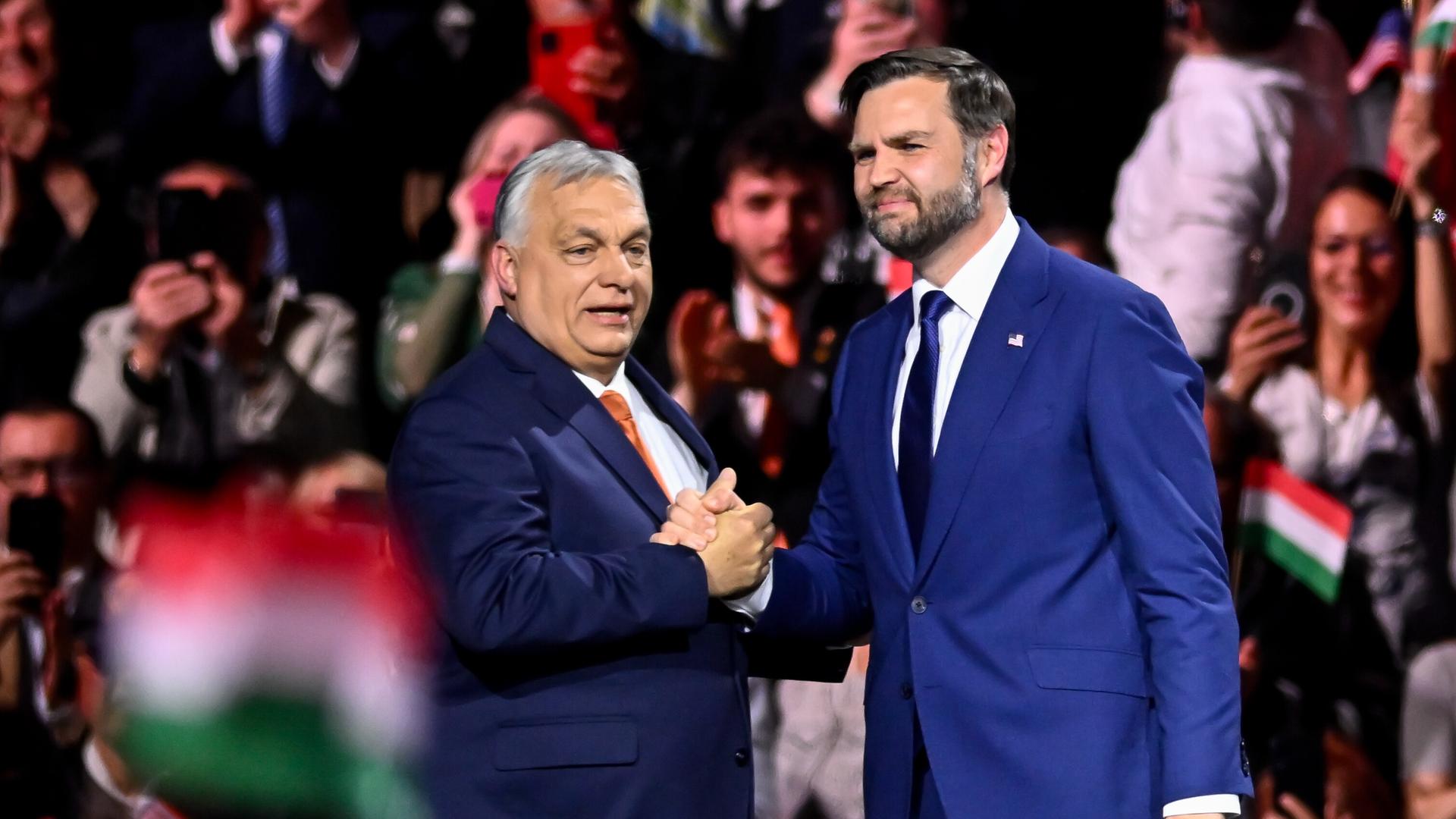 Viktor Orban und J.D. Vance schütteln Hände vor großem Publikum, das Ungarn-Fahnen schwenkt.