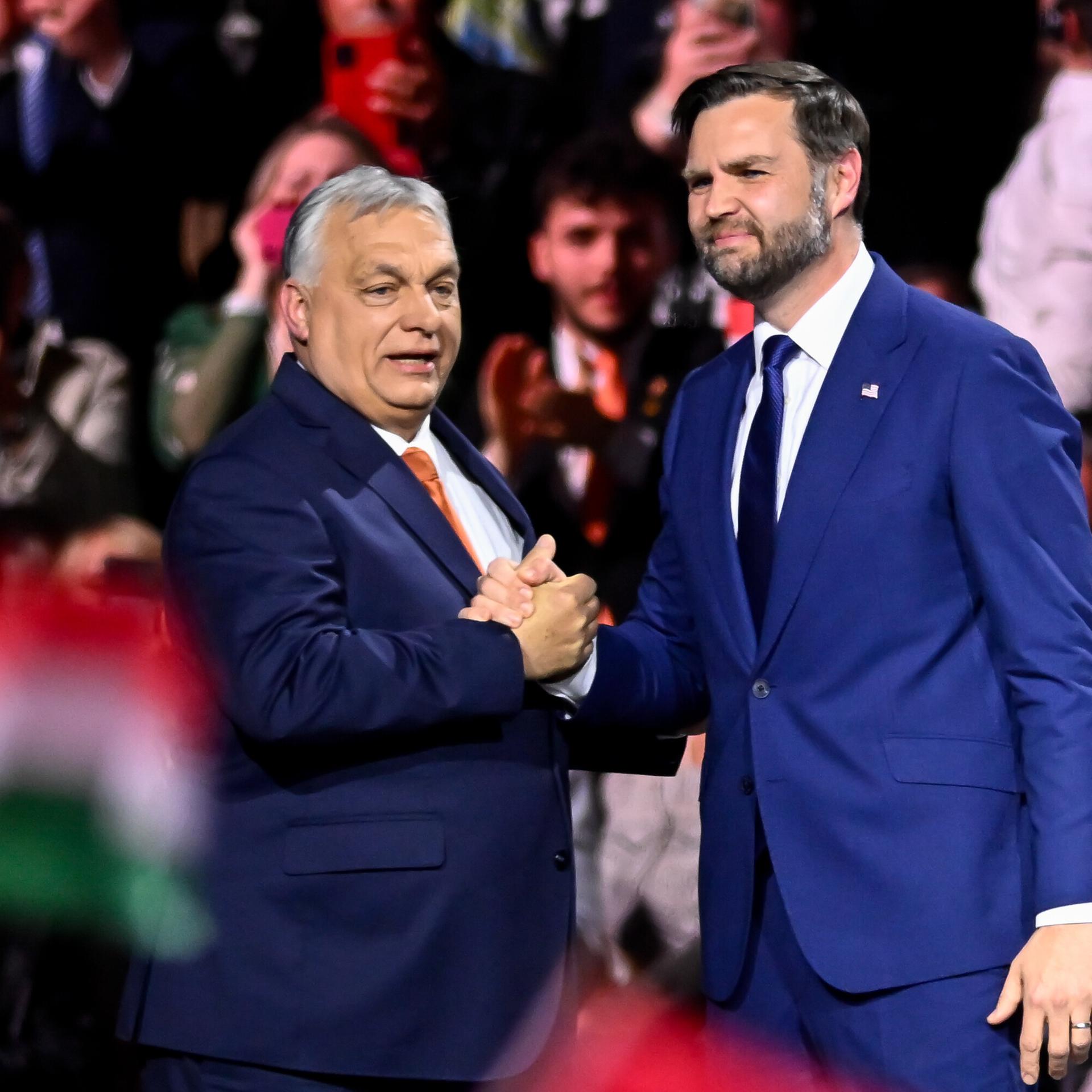 Viktor Orban und J.D. Vance schütteln Hände vor großem Publikum, das Ungarn-Fahnen schwenkt.
