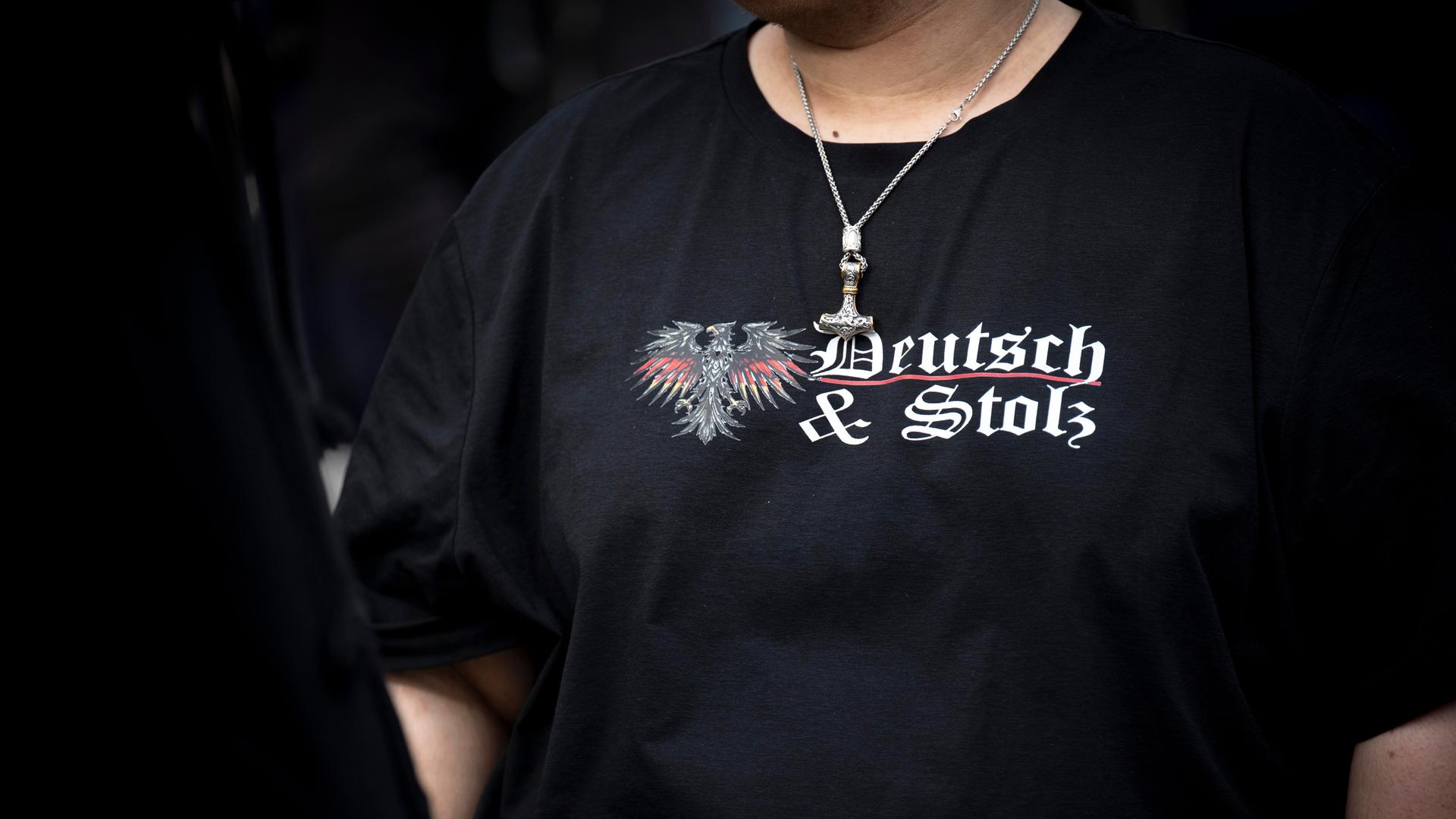 Ein junger männlicher Demonstrant trägt ein schwarzes Tshirt mit der Aufschrift "Deutsch und Stolz" sowie einen Kettenanhänger mit Reichsadler und Thorshammer bei einer Kundgebung der rechtsextremen Partei "Die Heimat", ehemals NPD. Berlin, März 2026