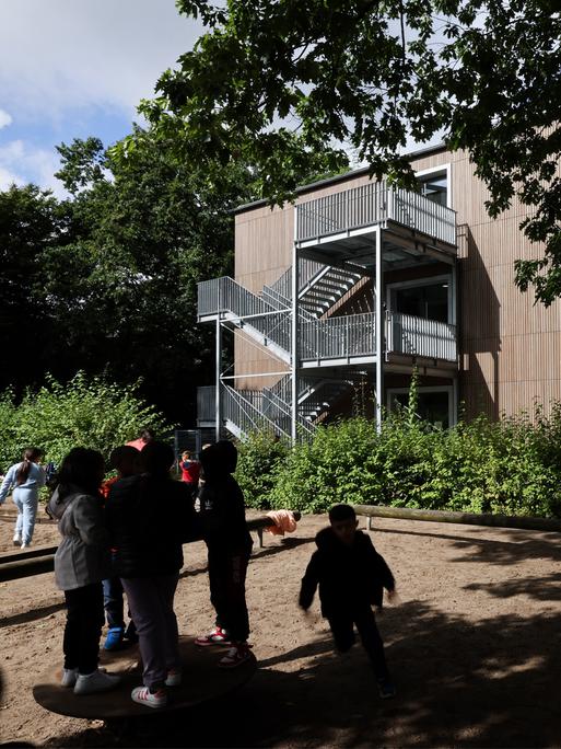 Blick auf ein Schulgebäude. Davor spielen Kinder im Schatten der Bäume. Blick auf ein Schulgebäude. Davor spielen Kinder im Schatten der Bäume.