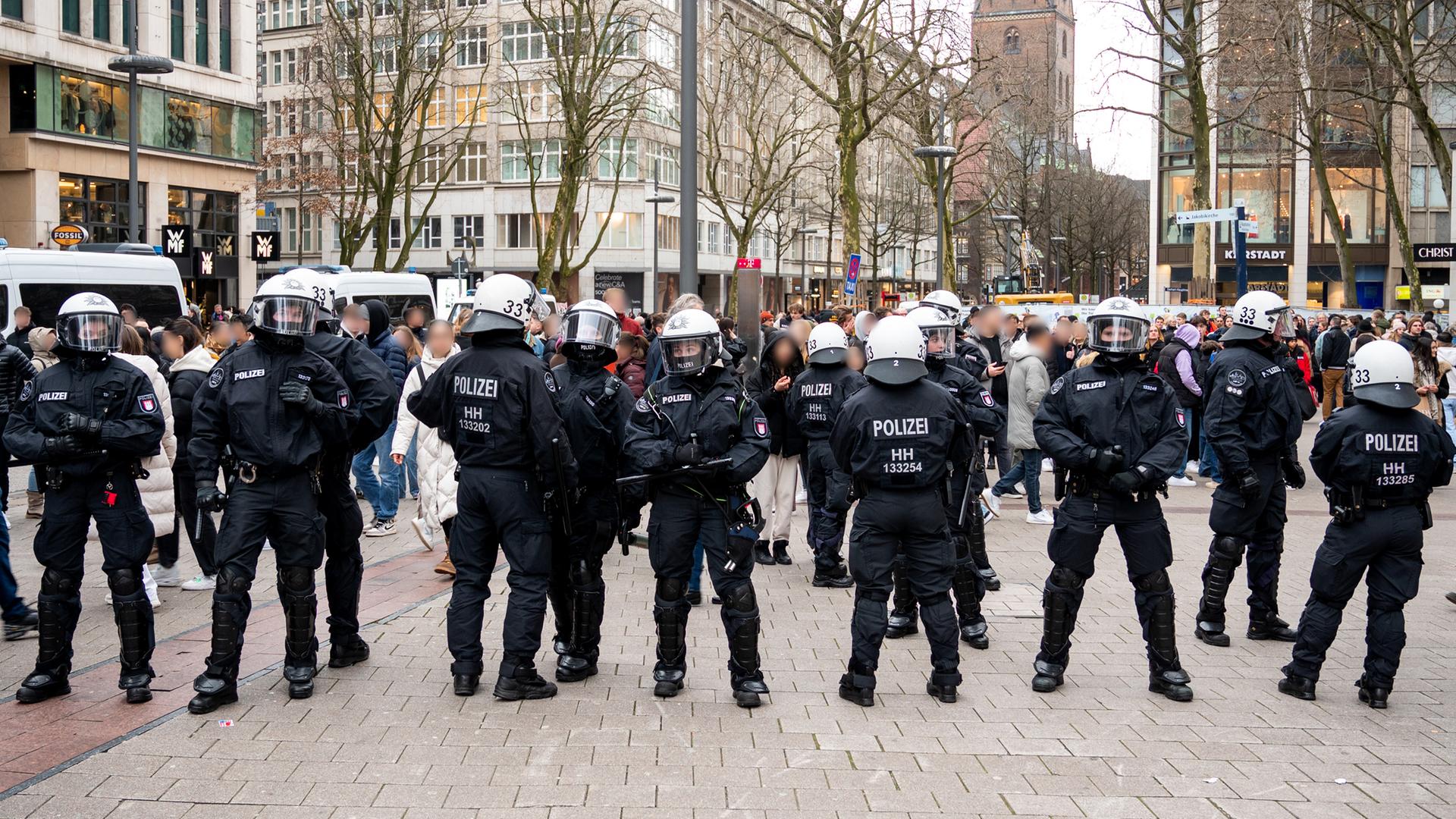Eine Kette von Polizisten in schwarzer Kampfmontur und weißen Helmen steht quer über den Platz. Dahinter viele Jugendliche.