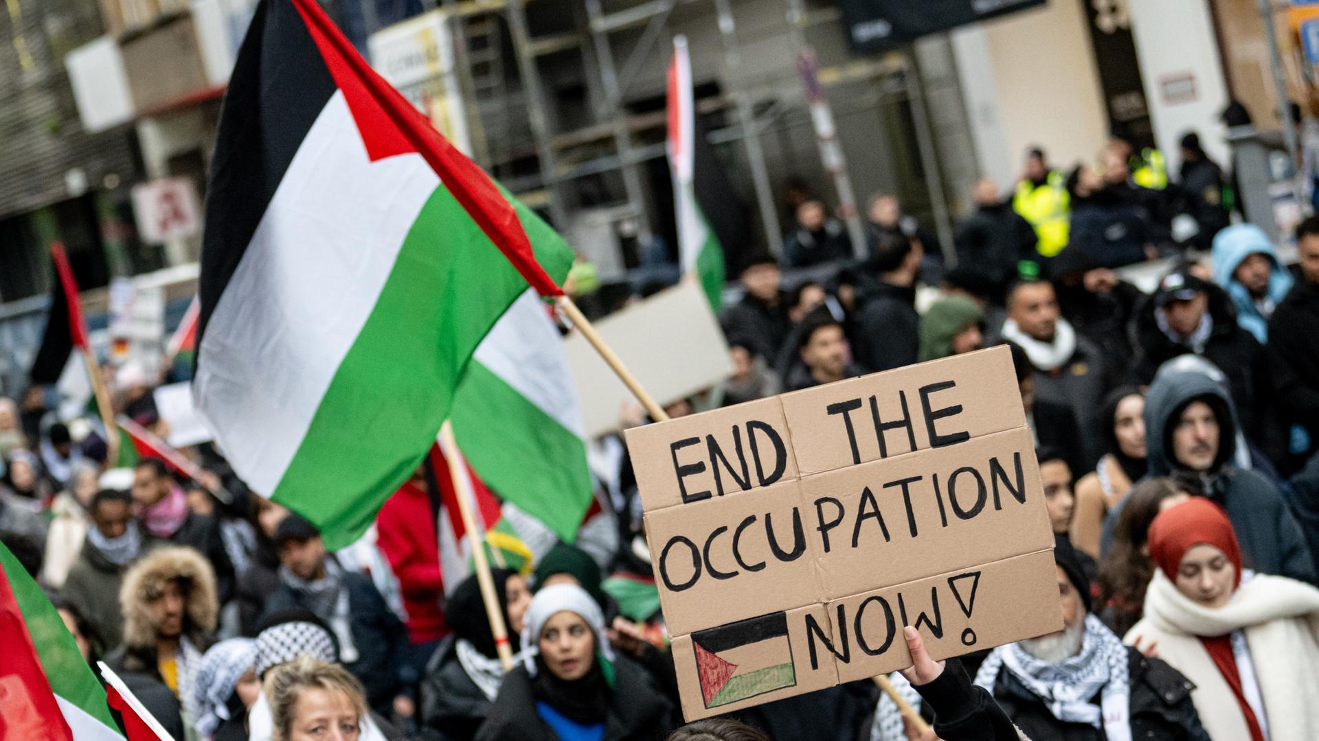 Menschen nehmen mit Schildern mit der Aufschrift "End the occupation now" an einer Demonstration für Palästina in Berlin-Mitte teil. Menschen nehmen mit Schildern mit der Aufschrift "End the occupation now" an einer Demonstration für Palästina in Berlin-Mitte teil.