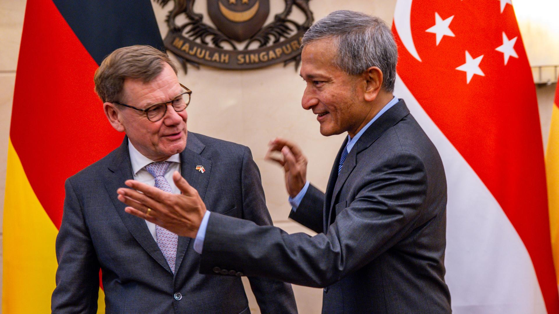 Die beiden stehen lächelnd in einem Raum nebeneinander. Balakrishnan weist Wadephul den Weg nach rechts. Dahinter die Flaggen beider Länder vor einer Wand. 