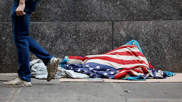 Vermutlich eine obachlose Person mit einer US-Flagge bedeckt, liegt auf einer Straße nahe der Wall Street. Aufgenommen am 18.6.2025 in New York City. 