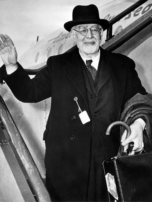 Eine Schwarzweiß-Fotografie zeigt einen älteren Mann mit schwarzem Hut, grüßend die Rolltreppe eines Flugzeugs herabsteigend. (Quelle: AP)