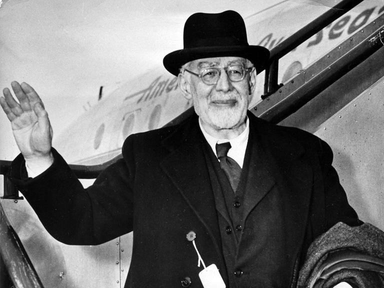 Eine Schwarzweiß-Fotografie zeigt einen älteren Mann mit schwarzem Hut, grüßend die Rolltreppe eines Flugzeugs herabsteigend. (Quelle: AP)