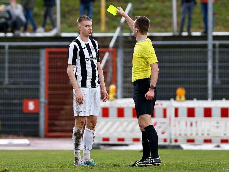 Ein Schiedsrichter zeigt einem Fußballspieler die Gelbe Karte.