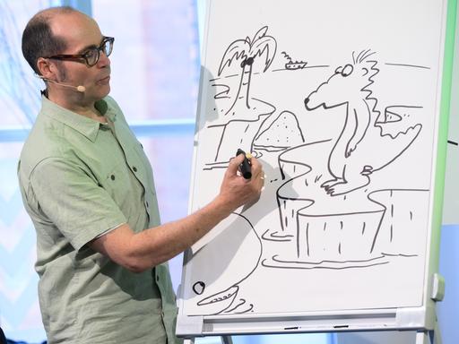 Kinderbuchautor Ingo Siegner zeigt, wie er seine Buchfigur Drache Kokosnuss zeichnet. Er steht vor einem Zeichenblock und zeichnet. Kinderbuchautor Ingo Siegner zeigt, wie er seine Buchfigur Drache Kokosnuss zeichnet. Er steht vor einem Zeichenblock und zeichnet.