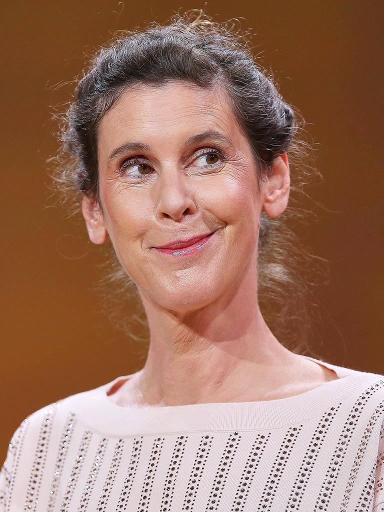 Daniela Dröscher steht vor einem neutralen Hintergrund, lächelt verschmitzt und blickt dabei ins Off