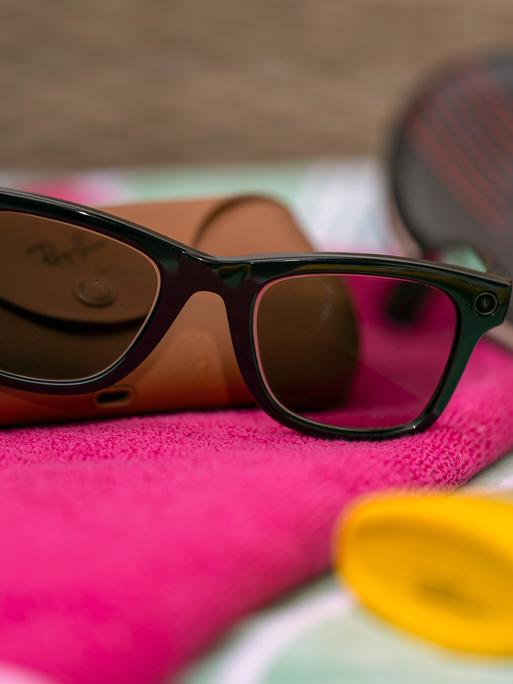 Eine Smart Glasses liegt auf einem Strandhandtuch zwischen Sonnencreme und Badelatschen. Eine Smart Glasses liegt auf einem Strandhandtuch zwischen Sonnencreme und Badelatschen.