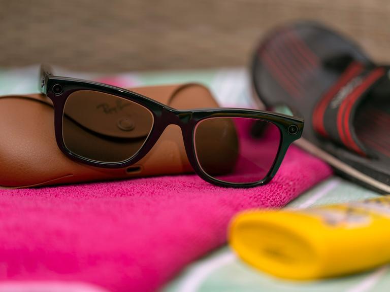Eine Smart Glasses liegt auf einem Strandhandtuch zwischen Sonnencreme und Badelatschen. Eine Smart Glasses liegt auf einem Strandhandtuch zwischen Sonnencreme und Badelatschen.