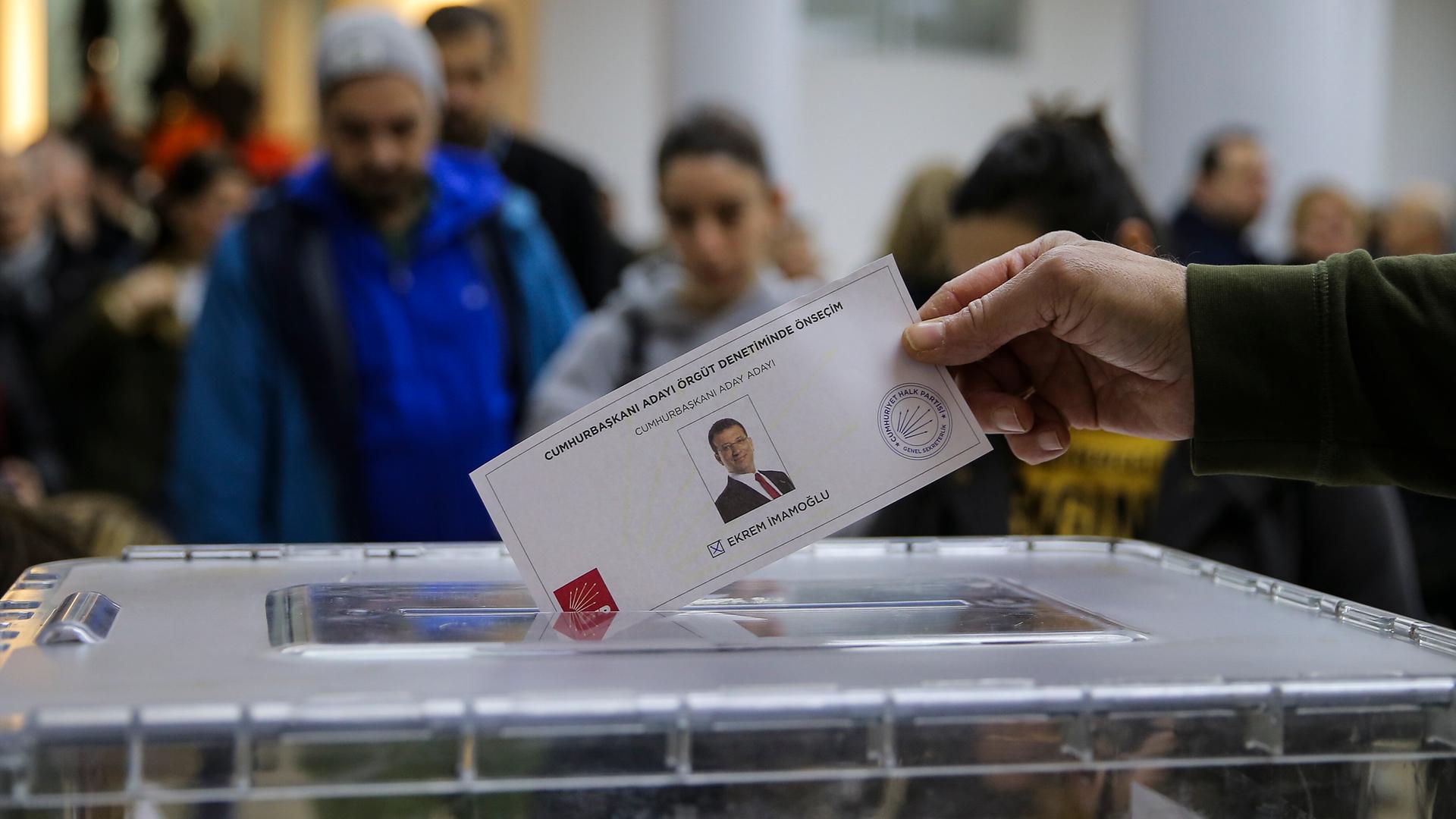 Eine Männerhand hält einen Zettel mit dem Bild des Oppositionspolitikers Imamoglu in der Hand und wirft ihn in einen Wahlurne. 