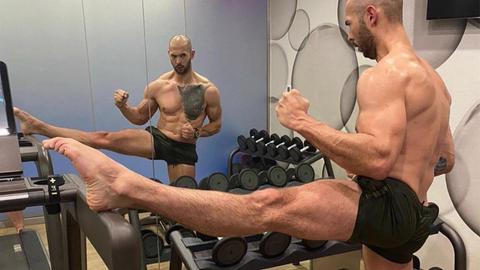 Andrew Tate in knapper kurzer Hose im Gym, er flext seine Muskeln und betrachtet sich im Spiegel.