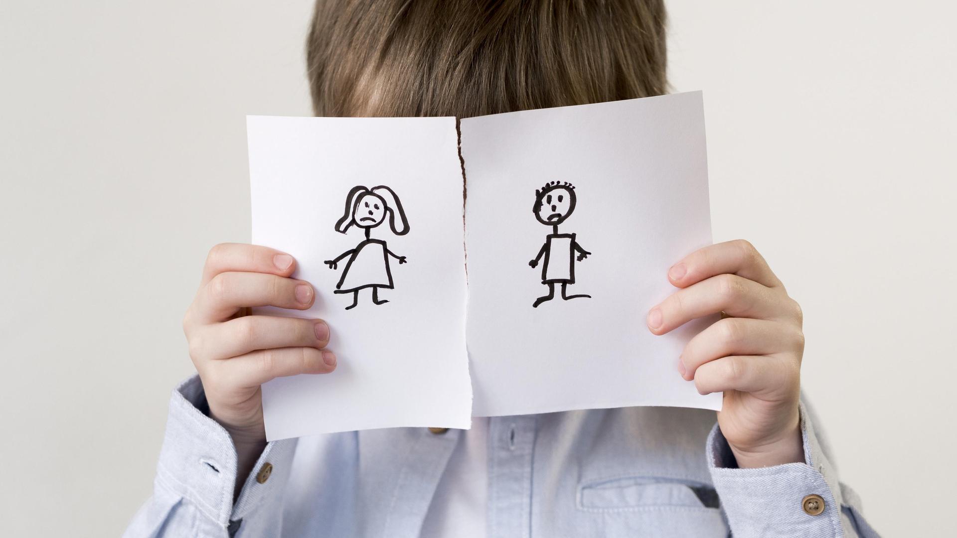 Ein Kind hält sich eine durchgerissene Zeichnung eines Paares vors Gesicht. (Symbolfoto)