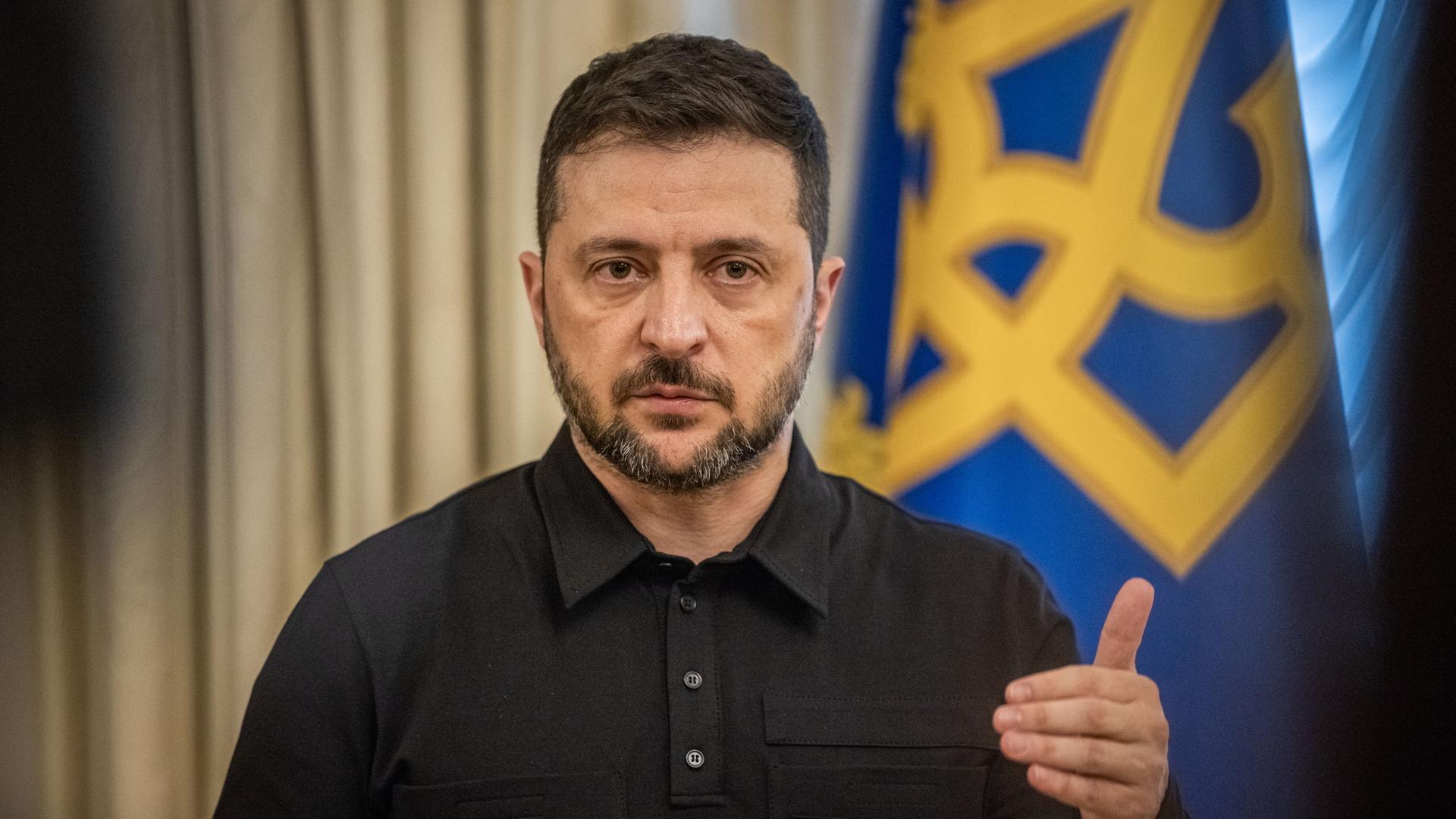 Wolodymyr Selenskyj steht gestikulierend vor einer ukrainischen Flagge