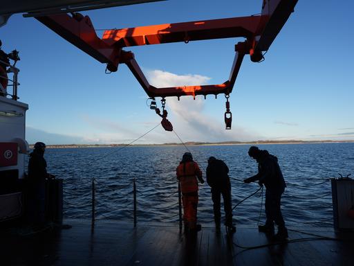 Besatzungsmitglieder ziehen in der Ostsee ein Kabel an Deck eines Forschungsschiffs. Mehr als fünf Jahre nach dem mysteriösen Verschwinden eines auf dem Grund fest verankerten Unterwasserobservatoriums gibt es neue Datensammler am Meeresgrund.