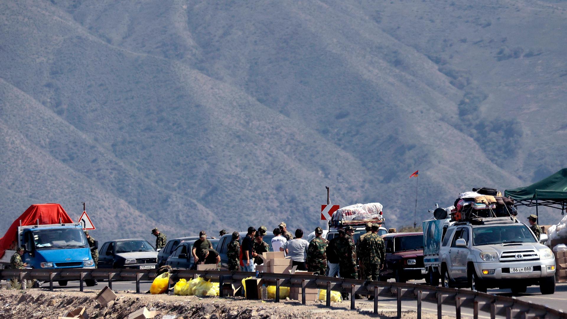 Flüchtlinge aus Bergkarabach: Autos und Menschen auf einer Straße, im Hintergrund Berge