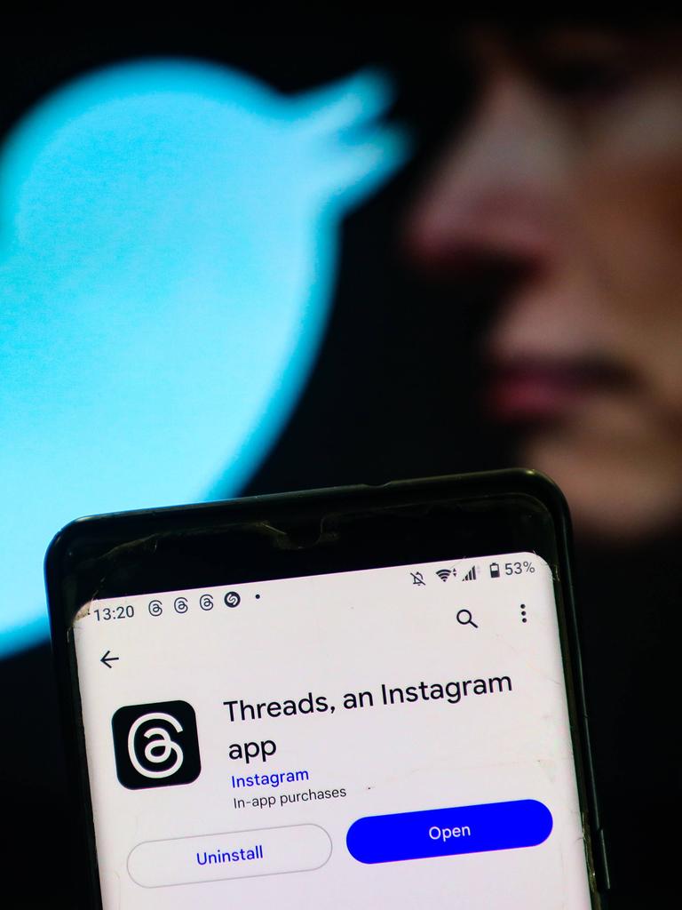 Zu sehen ist die App "Threads" auf einem Handy. Dahinter in der Unschärfe Elon Musk und das Twitter-Logo, der zwitschernde Vogel in hellem Blau.