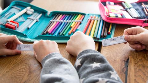 Zwei Schulkinder halten ihren SARS-CoV-2 Rapid Antigen Test in der Hand dieser Negativ anzeigt, im Hintergrund liegt eine Federmappe, Hefte und Bücher für die Schule auf dem Tisch.