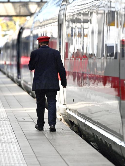 Ein Zugbegleiter der Detutschen Bahn geht an einem ICE entlang.