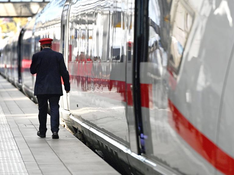 Ein Zugbegleiter der Detutschen Bahn geht an einem ICE entlang.