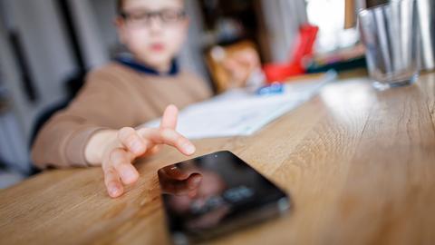 Ein Kind tippt auf einem Smartphone während es Hausaufgaben macht. (Gestellte Aufnahme) Ein Kind tippt auf einem Smartphone während es Hausaufgaben macht. (Gestellte Aufnahme)
