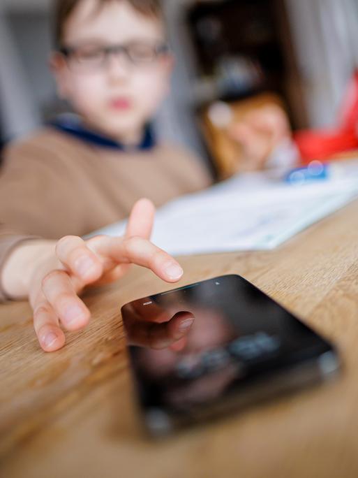 Ein Kind tippt auf einem Smartphone während es Hausaufgaben macht. (Gestellte Aufnahme)