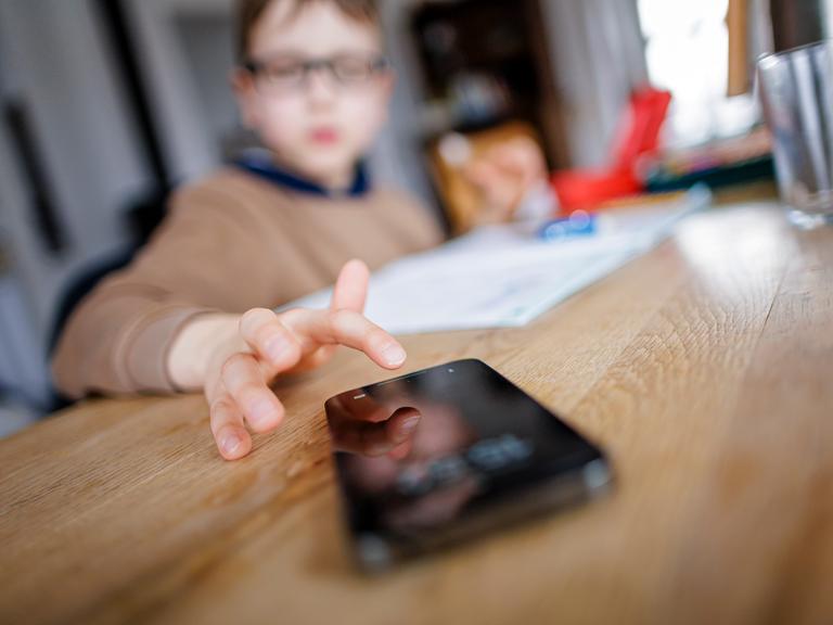 Ein Kind tippt auf einem Smartphone während es Hausaufgaben macht. (Gestellte Aufnahme)
