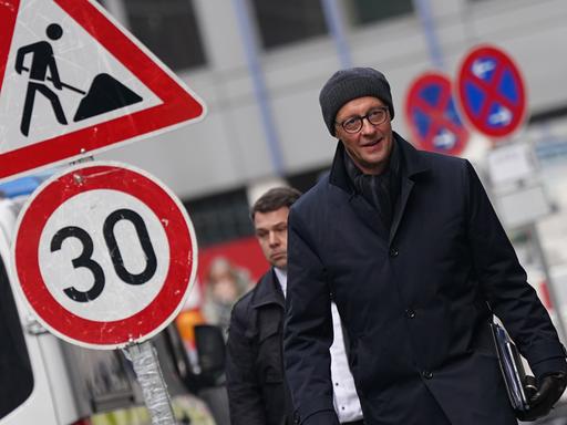 Friedrich Merz, Kanzlerkandidat und Parteivorsitzender der CDU, läuft auf einer winterlichen Straße entlang. Er trägt eine Mütze. Neben ihm ist ein Baustellenschild zu sehen, außerdem ein Schild zur Begrenzung des Tempolimits auf 30 Km/h. 