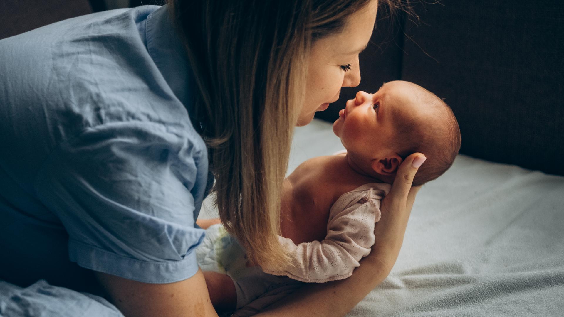 Ein neugeborenes Baby wird von seiner Mutter im Arm gehalten, die beiden schauen sich in die Augen.